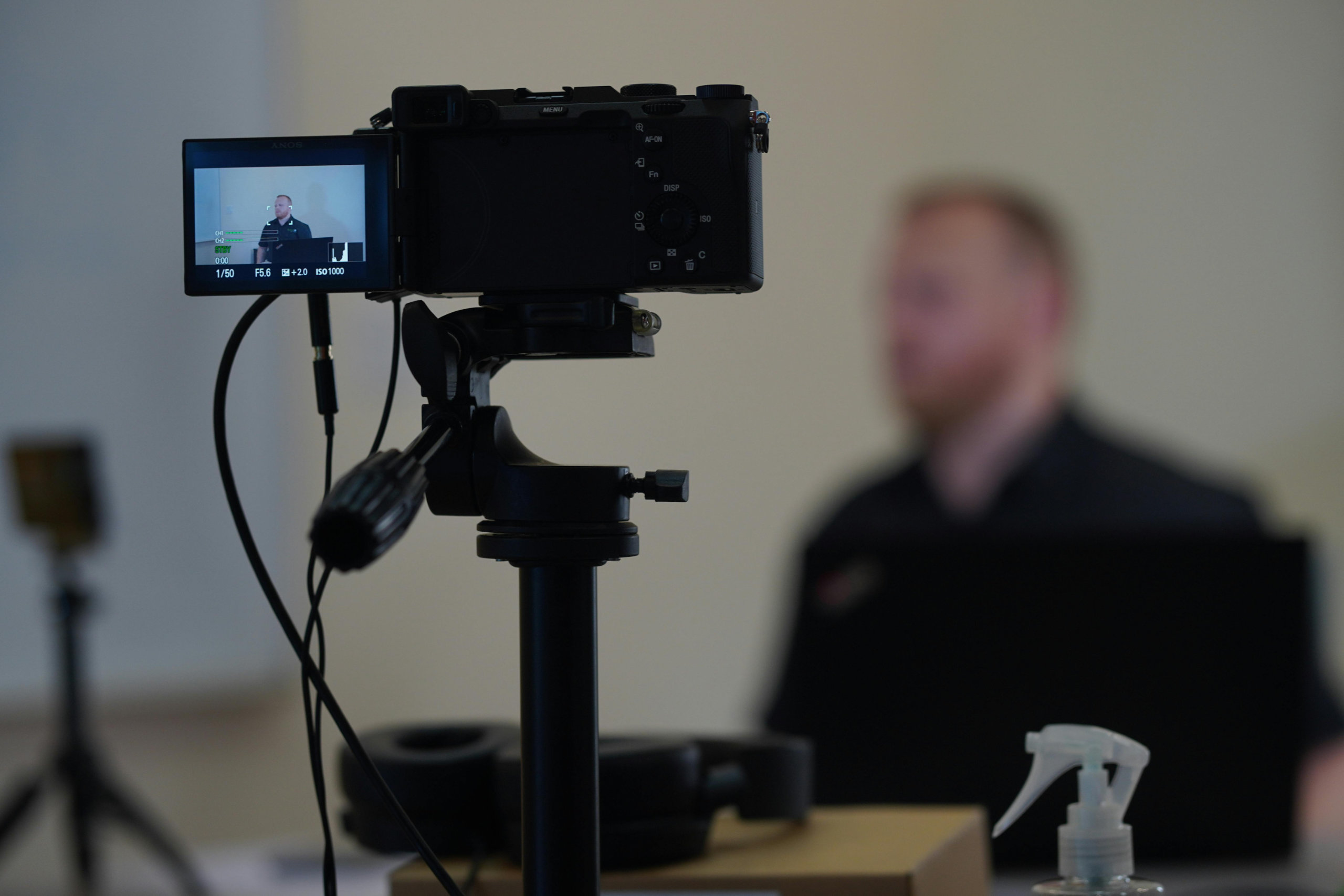 Eine Kamera in auf einem Stativ und auf einen Mann gerichtet der am Tisch sitzt