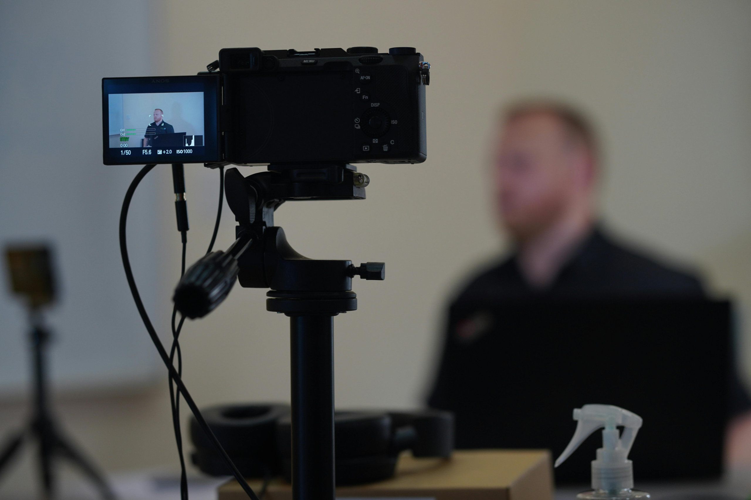 Eine Kamera in auf einem Stativ und auf einen Mann gerichtet der am Tisch sitzt